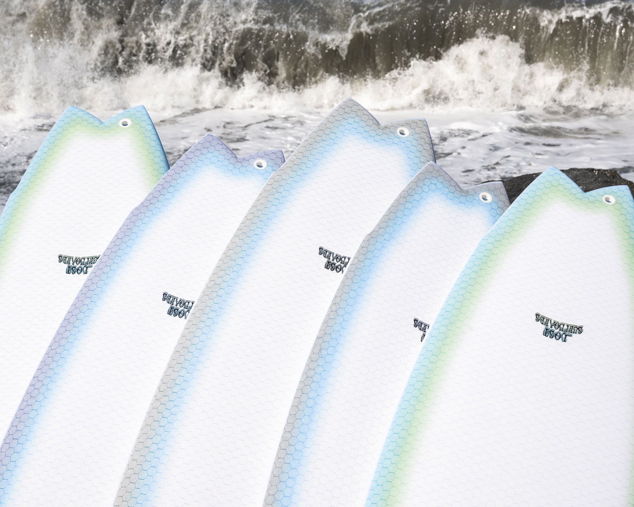 Fish tails of the Lib Tech x Mayhem Pisces surfboard, lined up on the beach.